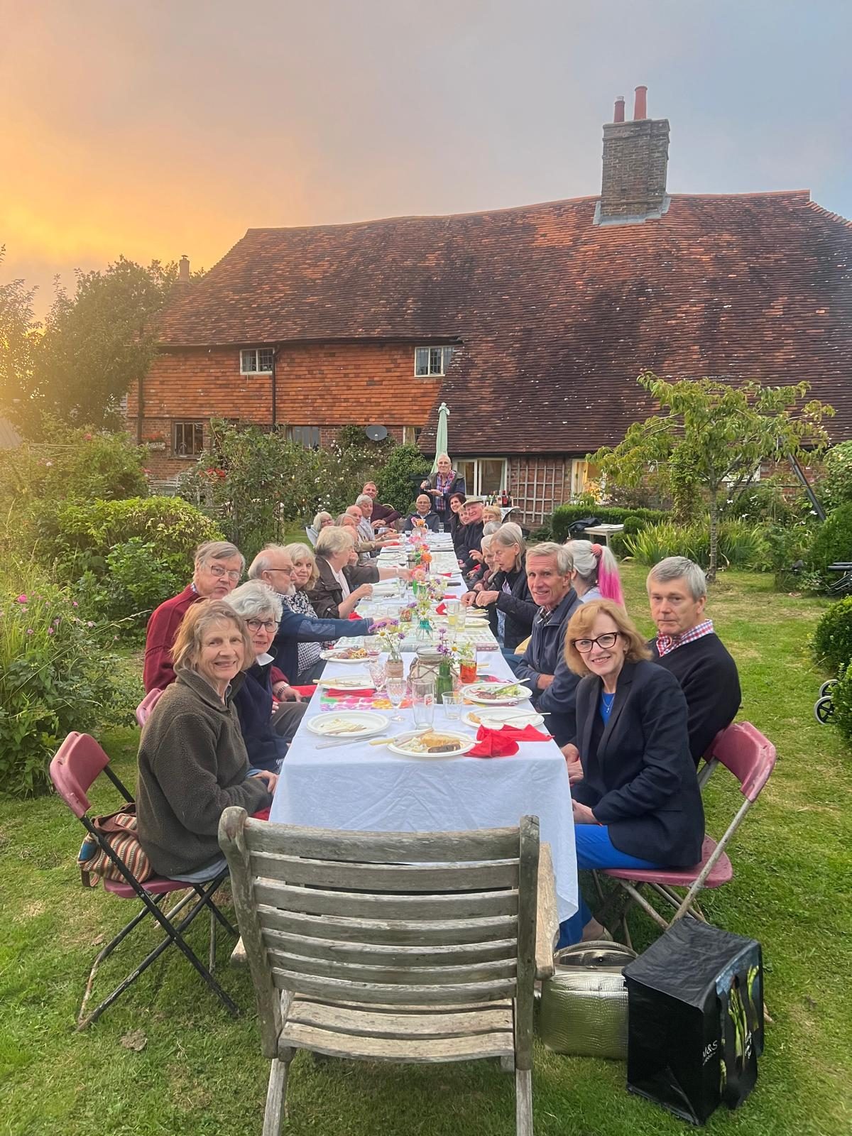 Club members and friends at a long table in a garden at sunset