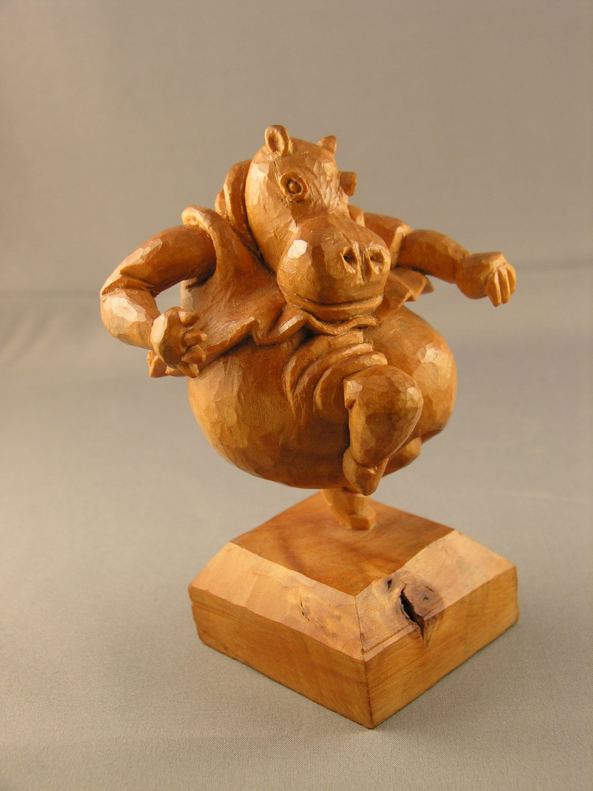 Carved hippo dancing on one leg on a wooden base