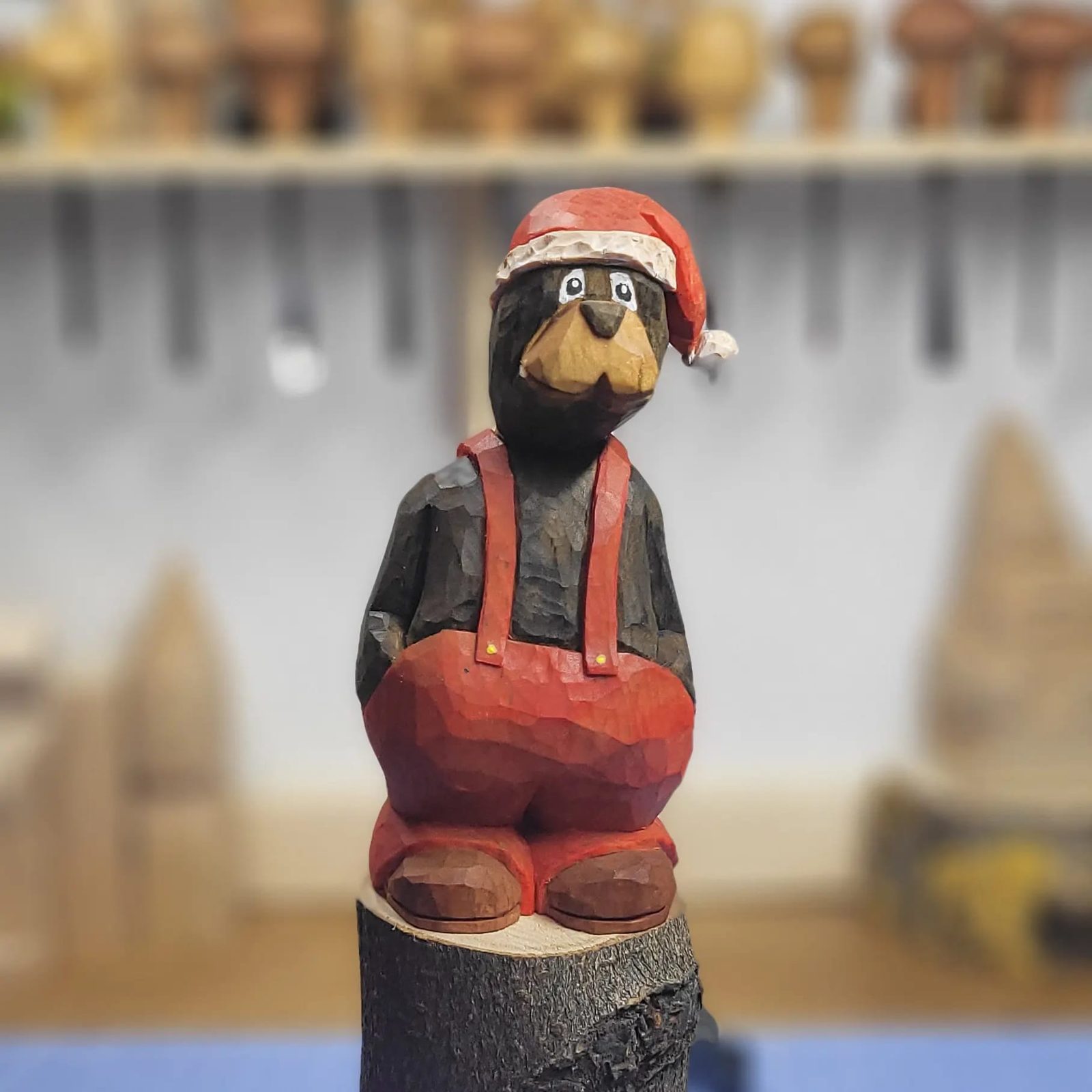 Painted caricature carving of a bear in a Santa hat and red dungarees