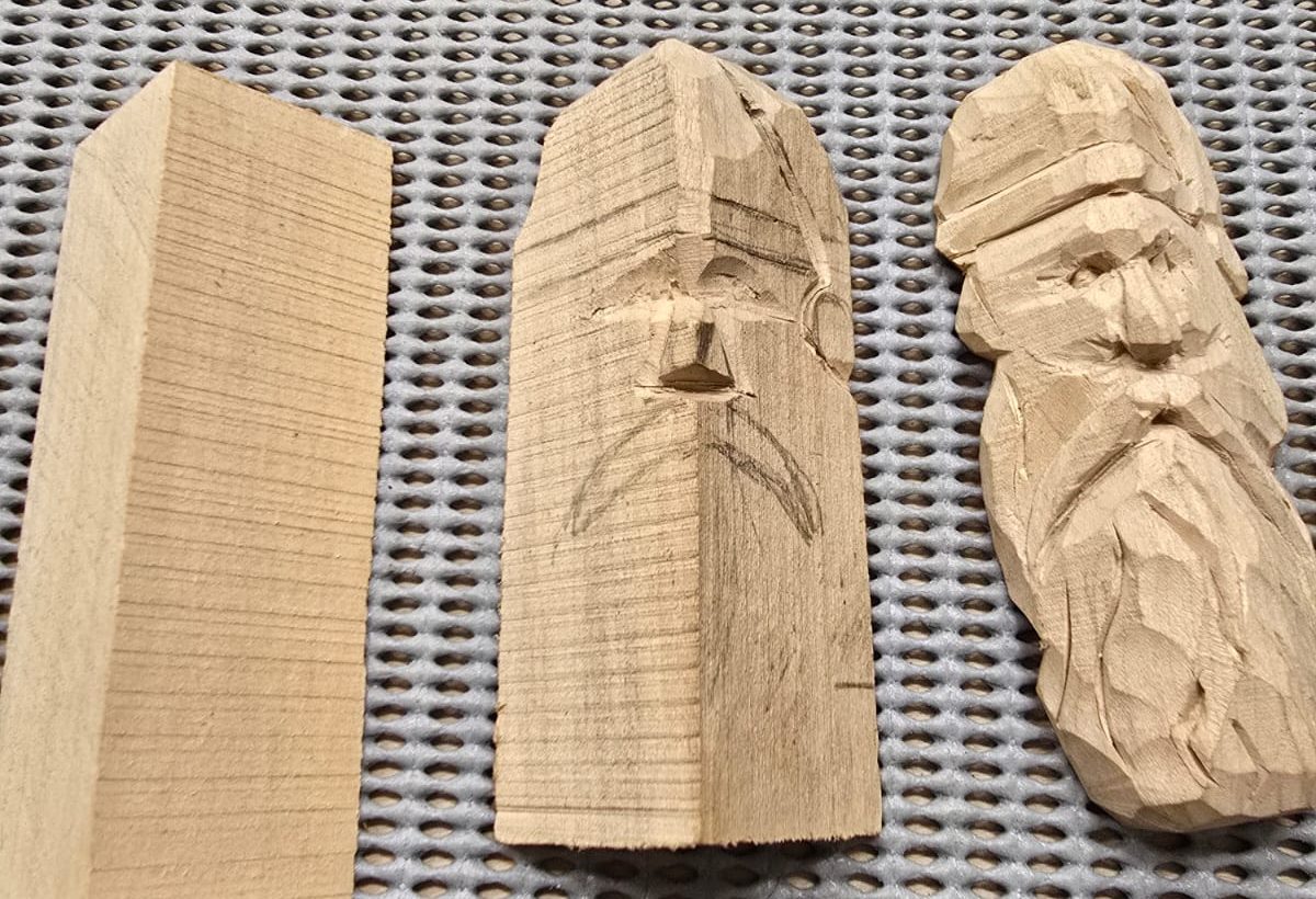 Three stages of a simple carved face: a plain block, a block with the face marked out and started, and the finished bearded face